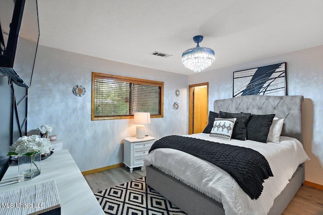 bedroom with hardwood / wood-style floors, a textured ceiling, and a chandelier