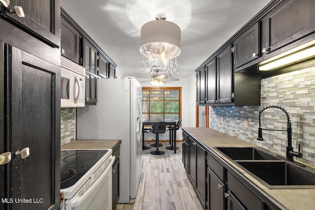 kitchen with hanging light fixtures, white appliances, sink, light hardwood / wood-style floors, and tasteful backsplash