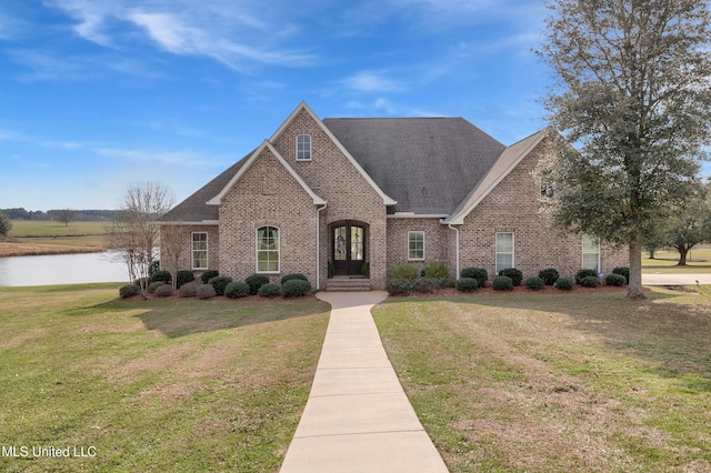 view of front facade with a water view, brick siding, a shingled roof, and a front yard