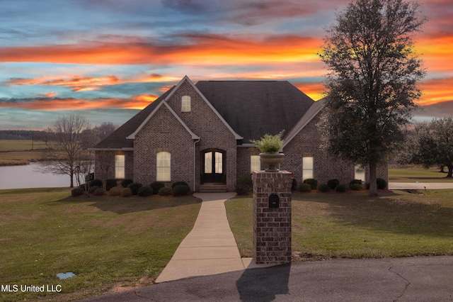 view of front facade featuring a shingled roof, a lawn, and brick siding