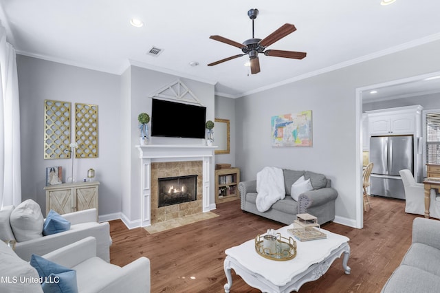 living room with crown molding, ceiling fan, dark hardwood / wood-style flooring, and a tile fireplace