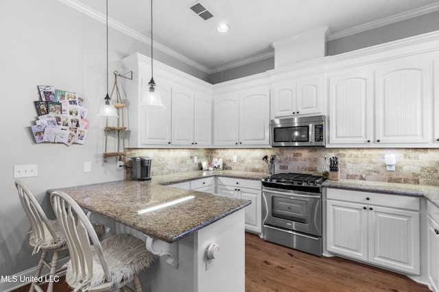 kitchen with a breakfast bar, decorative light fixtures, dark stone countertops, appliances with stainless steel finishes, and white cabinets