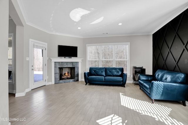 living room with a tiled fireplace, ornamental molding, and light hardwood / wood-style flooring