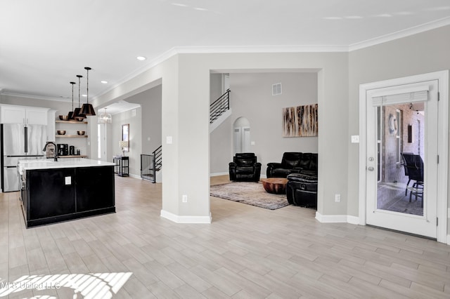 kitchen with crown molding, hanging light fixtures, a kitchen island with sink, white cabinets, and stainless steel fridge