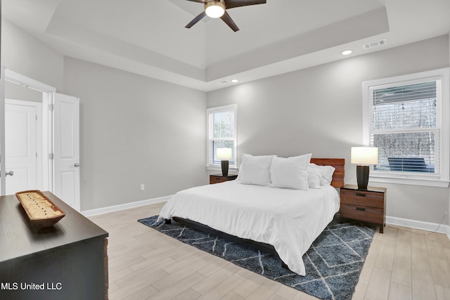 bedroom with ceiling fan, a tray ceiling, and light hardwood / wood-style flooring