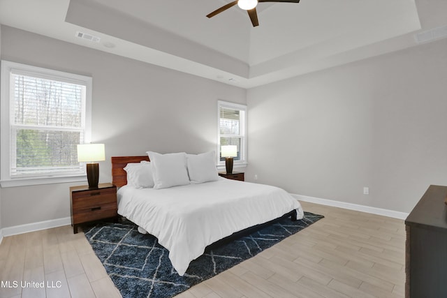 bedroom featuring light wood-type flooring, ceiling fan, and a tray ceiling