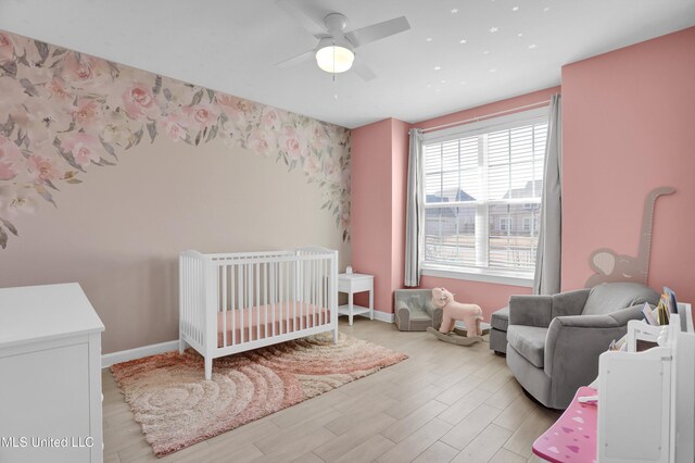 bedroom with light wood-type flooring, ceiling fan, and a nursery area