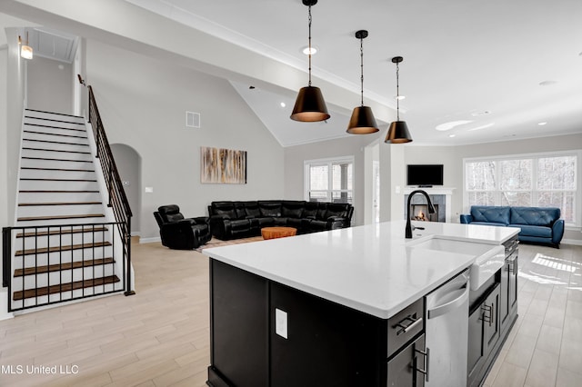 kitchen with light hardwood / wood-style floors, a kitchen island with sink, hanging light fixtures, stainless steel dishwasher, and sink