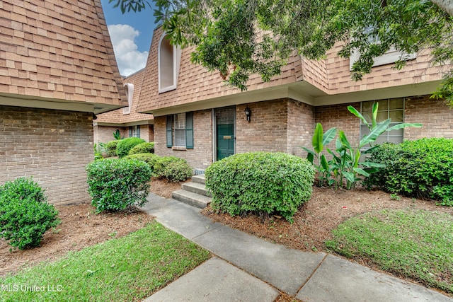 property entrance with mansard roof, a shingled roof, and brick siding