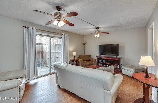 living room with a ceiling fan, light wood-style flooring, and a textured ceiling