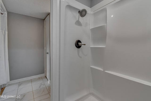 full bathroom featuring marble finish floors, a shower, baseboards, and a textured ceiling