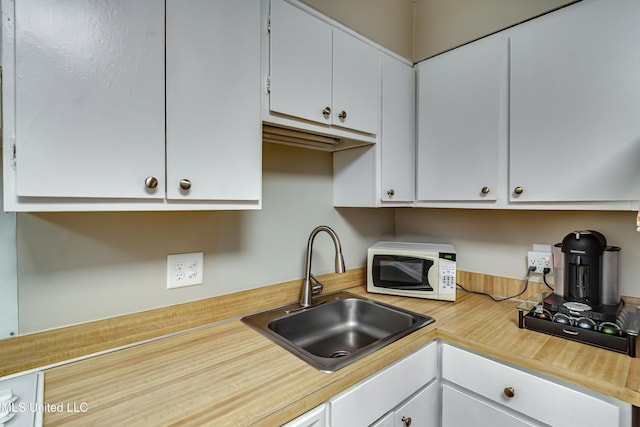 kitchen with white microwave, a sink, light countertops, and white cabinetry
