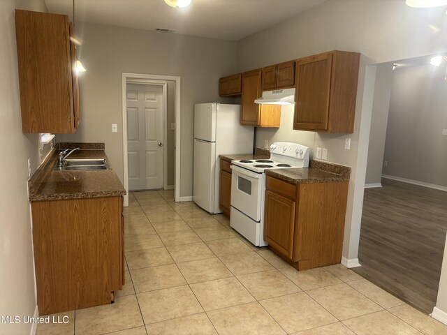 kitchen with under cabinet range hood, white appliances, dark countertops, and a sink