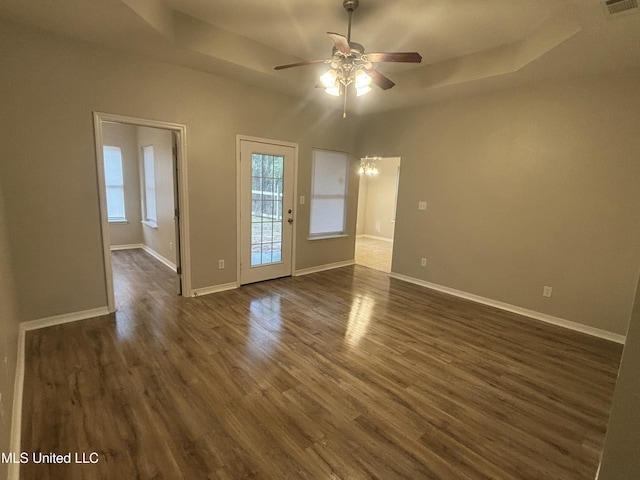 unfurnished room featuring dark wood finished floors, ceiling fan with notable chandelier, a raised ceiling, and baseboards