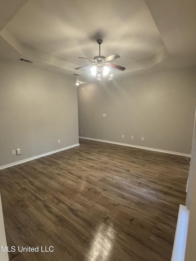 empty room with dark wood-style floors, visible vents, a ceiling fan, and baseboards