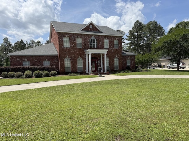 georgian-style home featuring roof with shingles, a front lawn, and brick siding