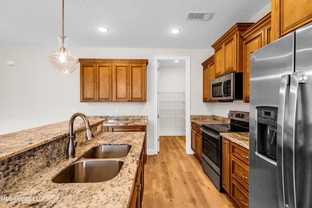 14864 Audubon Lake Blvd, Gulfport, MS 39503 - kitchen featuring stainless steel appliances, light wood-style floors, pendant lighting, brown cabinets, and light stone countertops