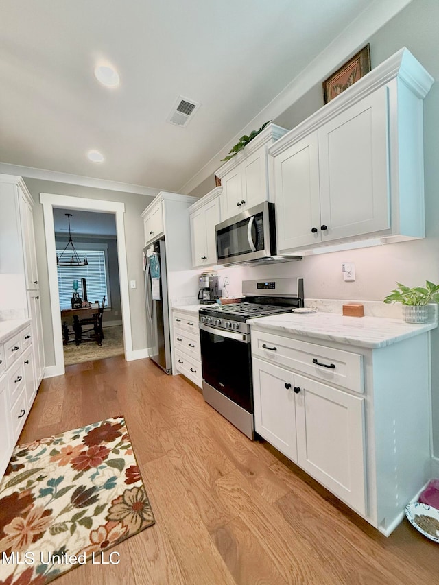 kitchen with white cabinetry, crown molding, light stone counters, appliances with stainless steel finishes, and light hardwood / wood-style floors