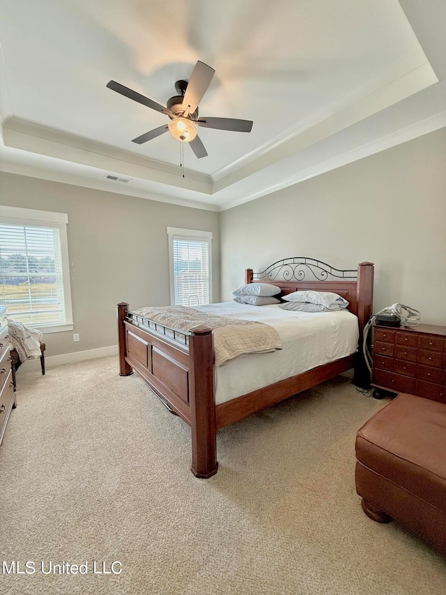 bedroom with multiple windows, light colored carpet, ceiling fan, and a tray ceiling