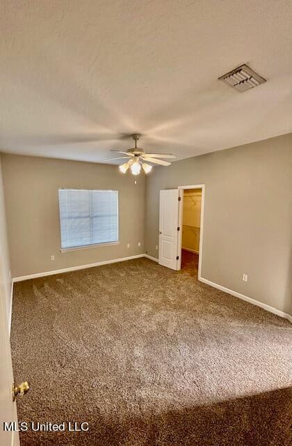 unfurnished bedroom featuring a closet, a spacious closet, carpet flooring, and ceiling fan