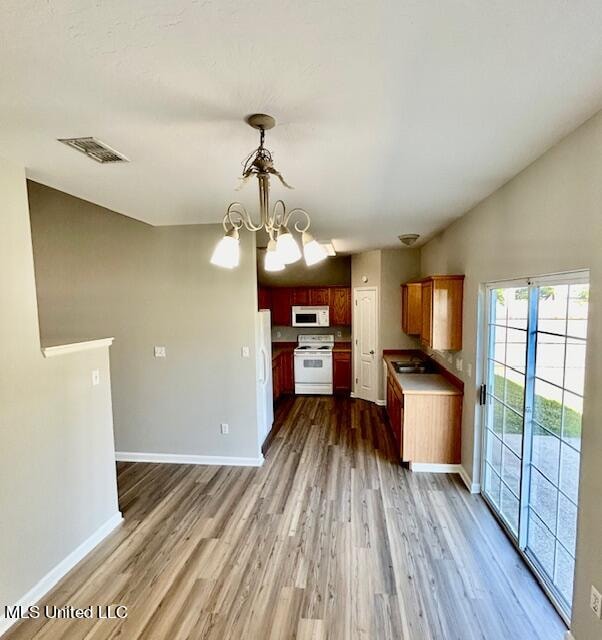 kitchen featuring an inviting chandelier, hardwood / wood-style flooring, vaulted ceiling, and white appliances