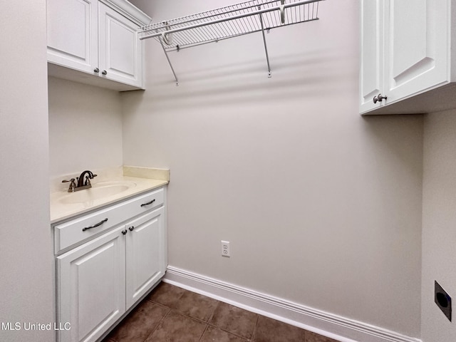 laundry room with electric dryer hookup, dark tile patterned floors, baseboards, and a sink