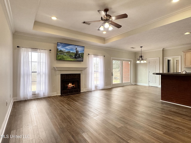 unfurnished living room with visible vents, a tray ceiling, ceiling fan with notable chandelier, a fireplace, and wood finished floors