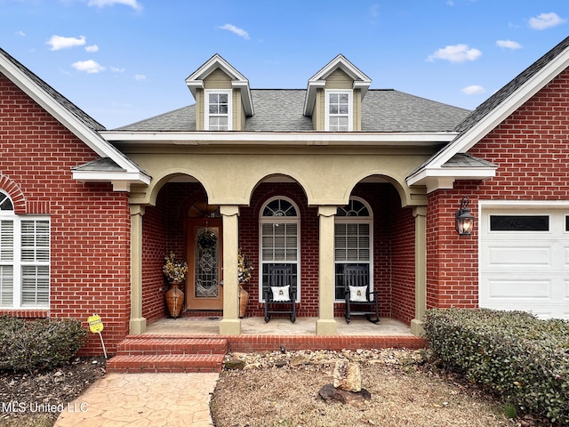 entrance to property featuring brick siding, covered porch, an attached garage, and a shingled roof