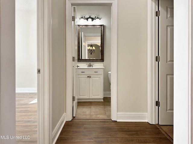 hallway with dark wood finished floors, baseboards, and a sink