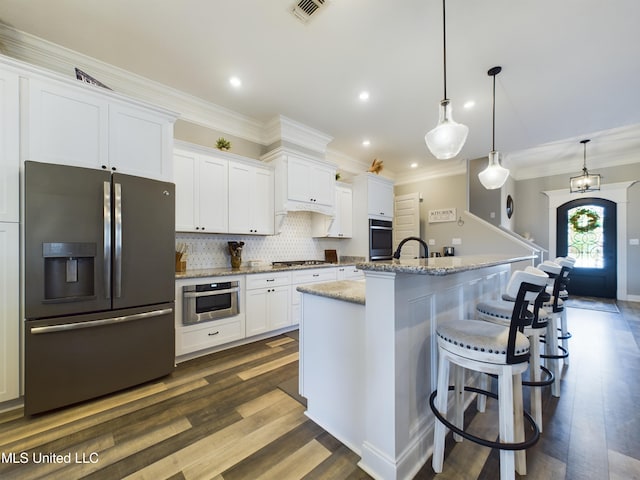 kitchen featuring a kitchen island with sink, hanging light fixtures, appliances with stainless steel finishes, light stone counters, and white cabinetry