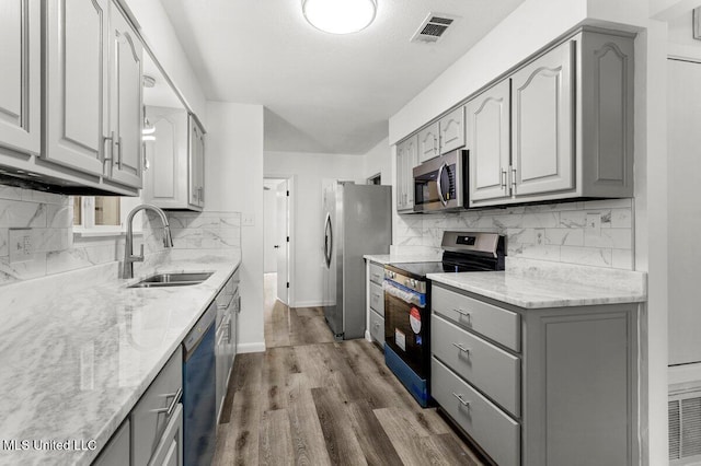 kitchen featuring sink, gray cabinets, appliances with stainless steel finishes, light stone counters, and wood-type flooring