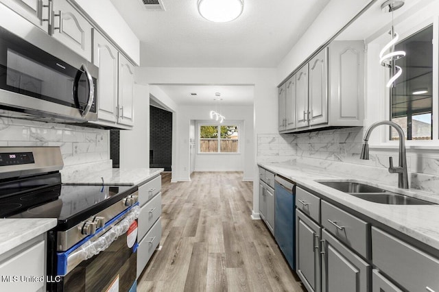 kitchen featuring sink, appliances with stainless steel finishes, gray cabinets, pendant lighting, and light stone countertops