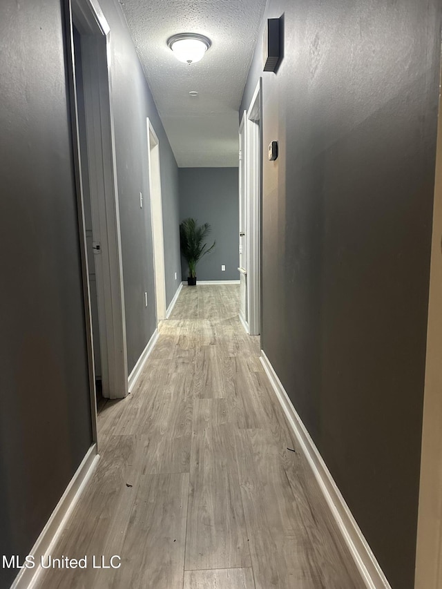 hallway with light hardwood / wood-style flooring and a textured ceiling