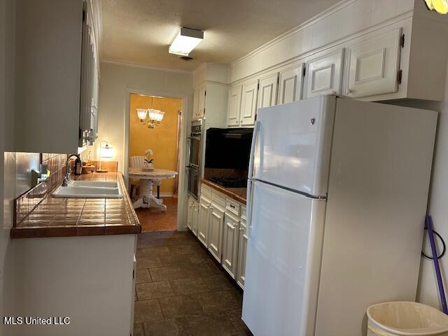 kitchen with tile countertops, white cabinetry, sink, and white fridge