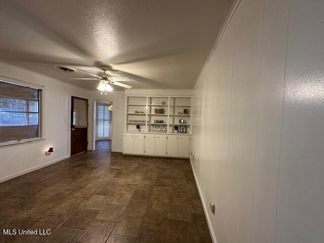 empty room with ceiling fan, built in features, and a textured ceiling