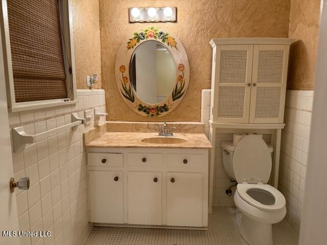 bathroom with tile patterned flooring, vanity, toilet, and tile walls