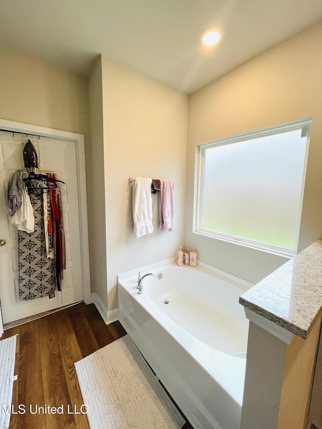 full bath featuring a bath, baseboards, a spacious closet, recessed lighting, and wood finished floors