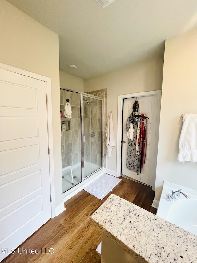 full bath with a tub to relax in, a walk in closet, a shower stall, and wood finished floors