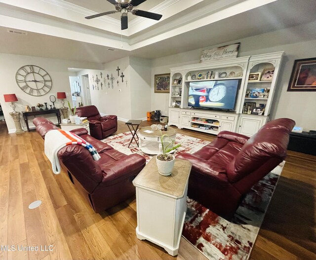 living room with light wood-type flooring, baseboards, a ceiling fan, crown molding, and a raised ceiling