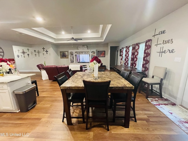 dining room with a raised ceiling, light wood-style floors, crown molding, baseboards, and ceiling fan