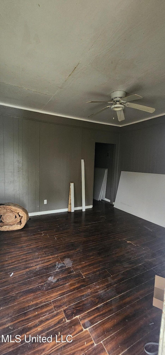 unfurnished room with wood walls, dark wood-type flooring, and ceiling fan