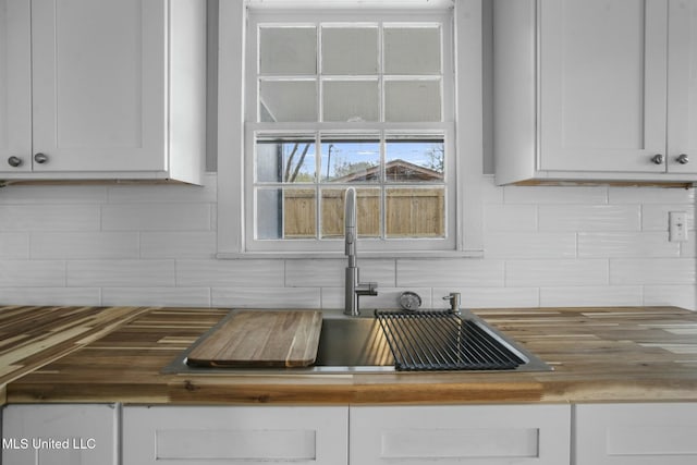 kitchen featuring sink, butcher block countertops, backsplash, and white cabinets