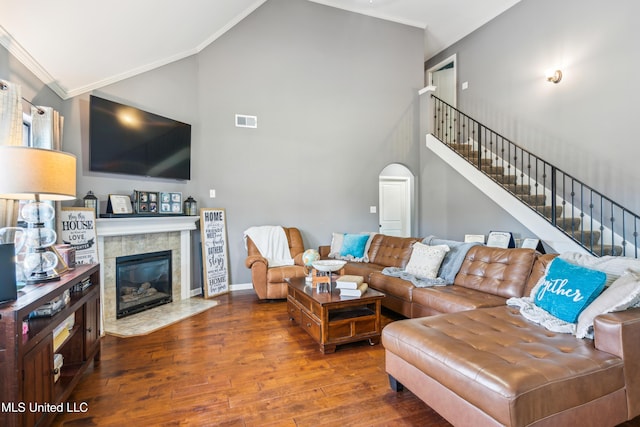 living room featuring dark hardwood / wood-style flooring, crown molding, a tiled fireplace, and vaulted ceiling