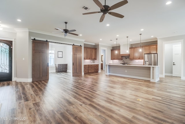 unfurnished living room featuring light wood-type flooring, a sink, a barn door, ceiling fan, and visible vents
