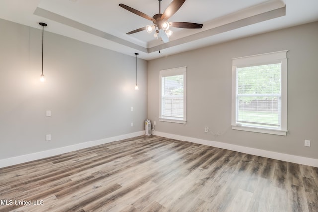 empty room featuring baseboards, plenty of natural light, a ceiling fan, and a raised ceiling