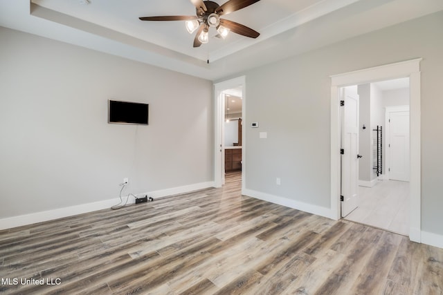 interior space with a tray ceiling, baseboards, wood finished floors, and ceiling fan