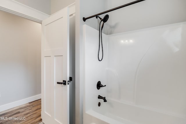 bathroom featuring baseboards, wood finished floors, and shower / bath combination