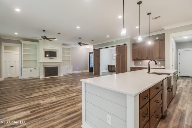 kitchen featuring light countertops, a kitchen island with sink, a ceiling fan, a barn door, and dark wood-style floors