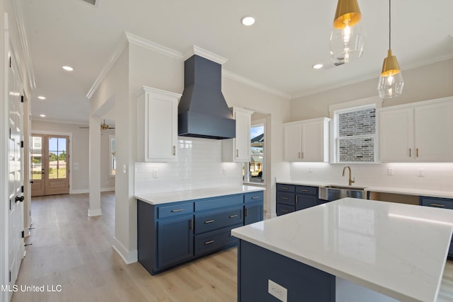 kitchen featuring premium range hood, white cabinetry, light wood-type flooring, sink, and a center island