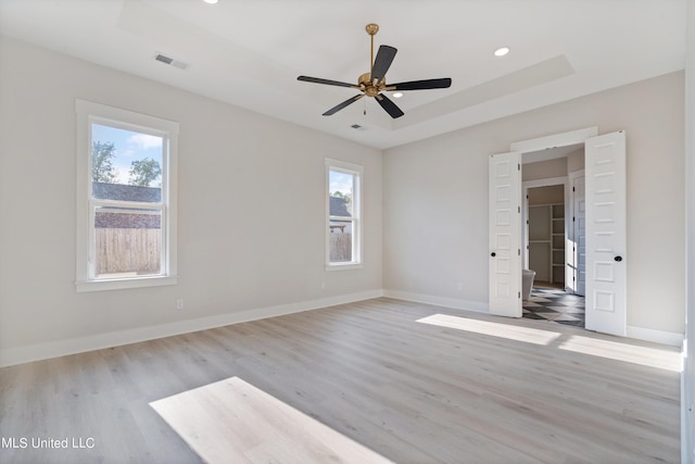 empty room with a wealth of natural light, a tray ceiling, light hardwood / wood-style floors, and ceiling fan